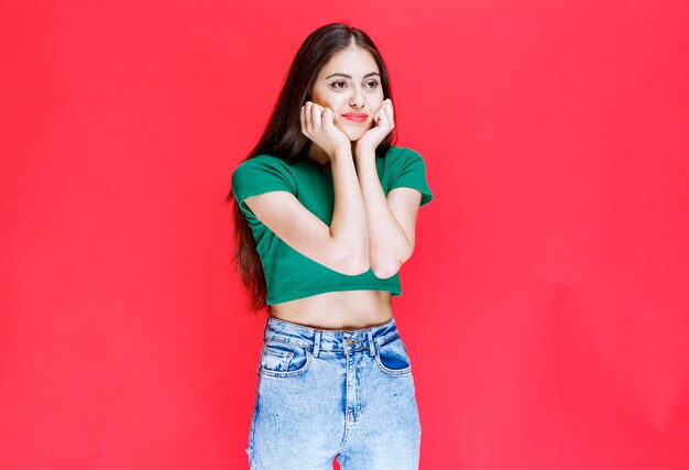 Foto de hermosa joven de pie con expresión feliz sobre fondo rojo.