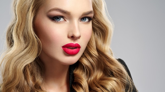 Foto de una hermosa joven rubia con labios rojos sexy. Closeup atractivo rostro sensual de mujer blanca con pelo largo. Maquillaje de ojos ahumados