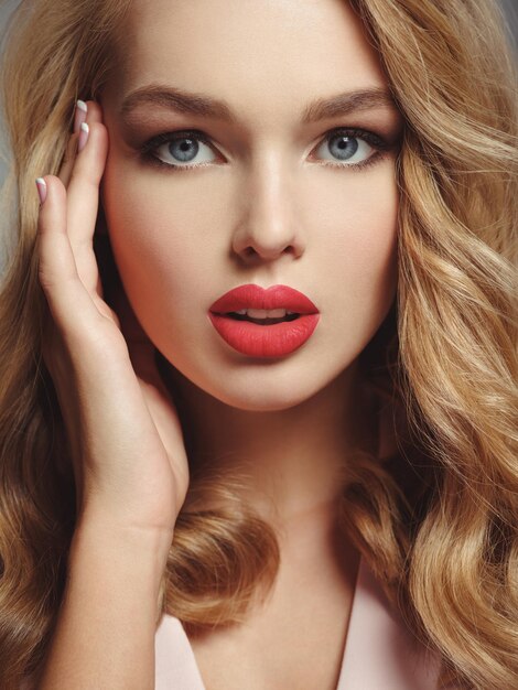 Foto de una hermosa joven rubia con labios rojos sexy. Primer atractivo rostro sensual de mujer blanca con pelo largo y rizado.