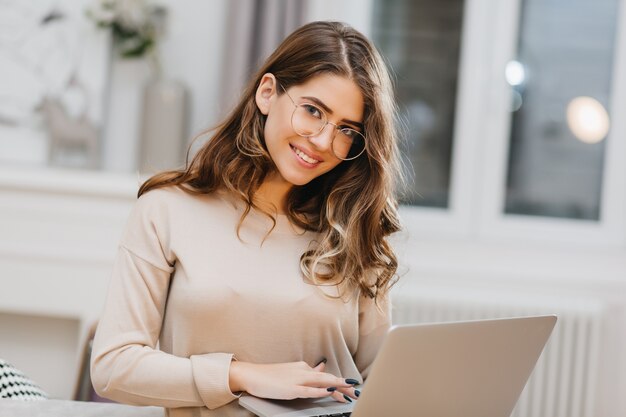 Foto de hermosa mujer blanca con gafas usando computadora con sonrisa encantadora