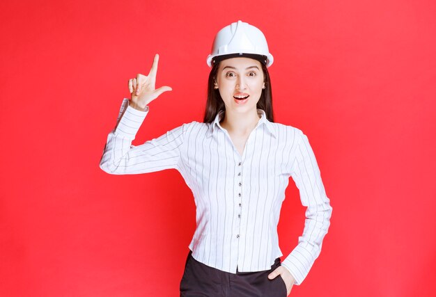 Foto de una hermosa mujer de negocios con sombrero de seguridad apuntando hacia afuera con los dedos.