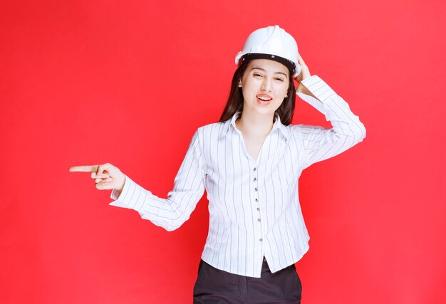 Foto de una hermosa mujer de negocios con sombrero de seguridad apuntando hacia afuera con los dedos.