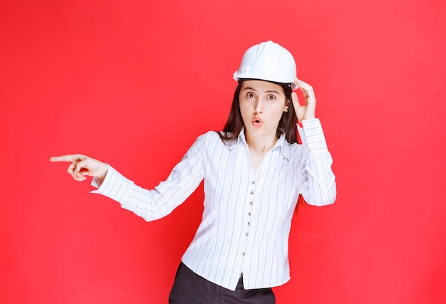 Foto gratuita foto de una hermosa mujer de negocios con sombrero de seguridad apuntando hacia afuera con los dedos.