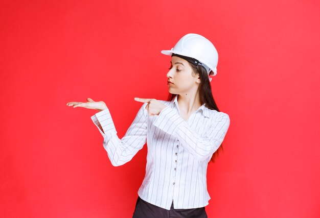 Foto de una hermosa mujer de negocios con sombrero de seguridad apuntando hacia afuera con los dedos.