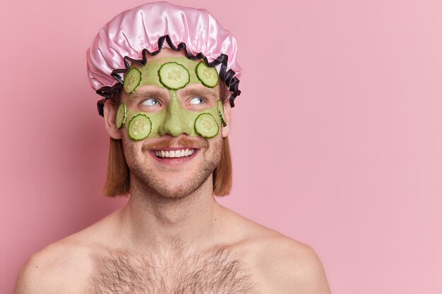 Foto de hombre sin afeitar satisfecho con máscara de pepino verde en la cara se somete a tratamientos de belleza disfruta de la rutina de cuidado de la piel