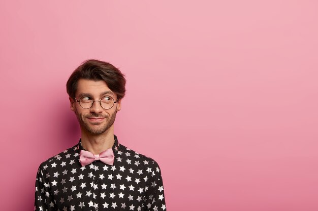 Foto de hombre alegre guapo con peinado de moda, mira a un lado, lleva gafas ópticas