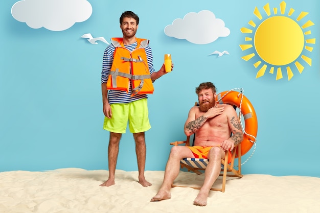 Foto gratuita foto de hombre alegre sugiere que un amigo usa protector solar, tiene una sonrisa positiva, usa chaleco salvavidas