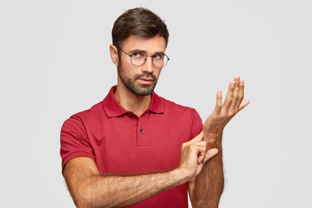 Foto de hombre atractivo usa anteojos redondos, mantiene la mano en la muñeca