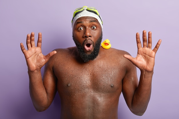 Foto de hombre emocionado que comparte impresiones después de bucear en el mar, gestos con ambas manos, como muestra qué pez grande vio bajo el agua, tiene gafas en la frente, pato de goma en el hombro