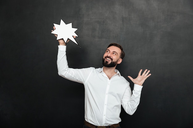 Foto del hombre encantado con estrella de discurso en blanco y mirando a un lado sobre la pared gris oscuro, copie el espacio