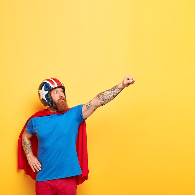 Foto de hombre fuerte con expresión seria, aprieta el puño y hace un gesto de vuelo, usa casco