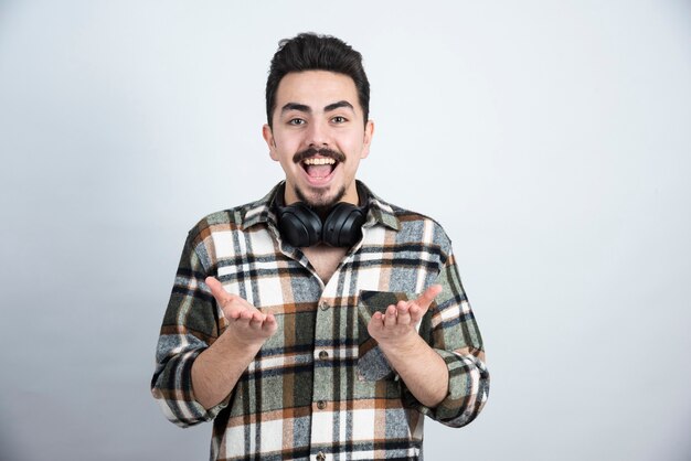 Foto de hombre guapo con auriculares de pie y mirando por encima de la pared blanca.