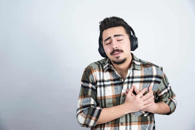 Foto de hombre guapo con auriculares sosteniendo a sí mismo sobre la pared blanca.