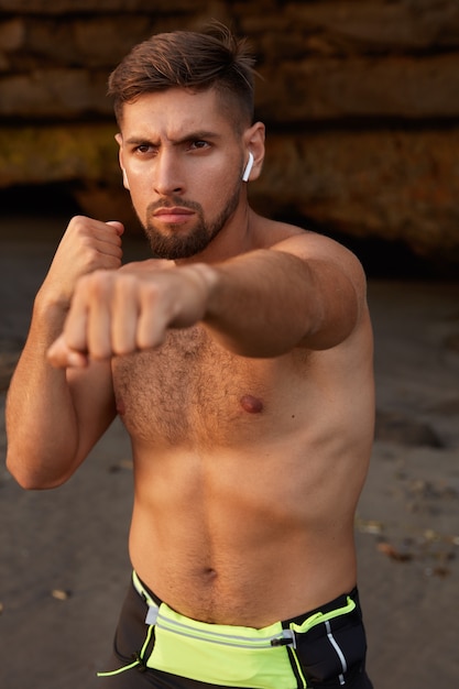 Foto gratuita foto de hombre guapo de masculinidad levanta los puños cerrados en ataque, hace ejercicio de boxeo