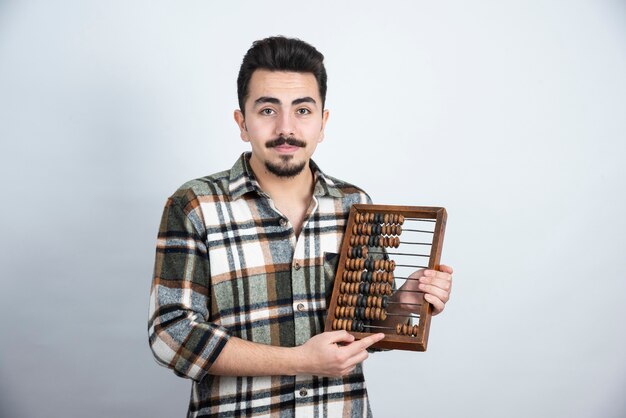 Foto de hombre joven con cuentas de madera de pie sobre una pared blanca.