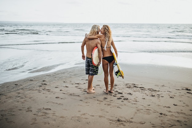 Foto de un hombre y una mujer en trajes de baño sosteniendo tablas de surf contra el mar
