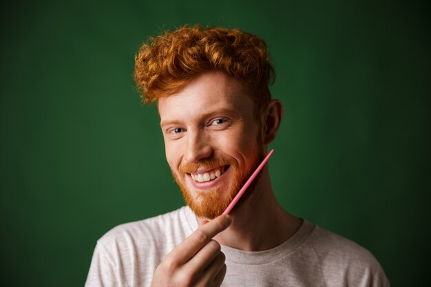 Foto de hombre sonriente cabeza lectora, peinándose la barba con peine rosa