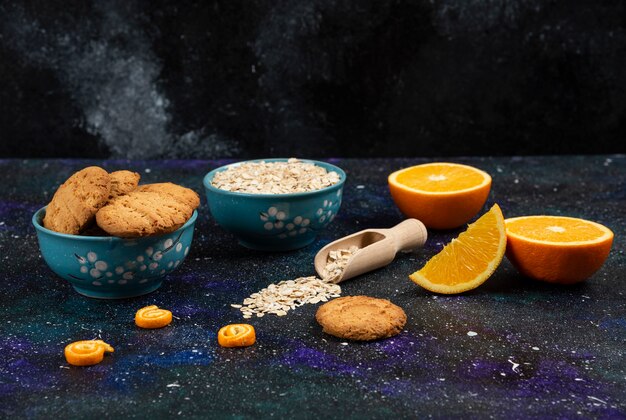 Foto horizontal de galletas y avena en tazones, medio cortado y en rodajas de orang eon molido.