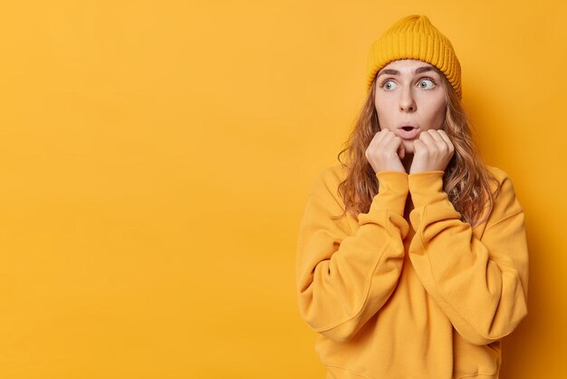 Una foto horizontal de una joven asustada y conmocionada mantiene las manos en la cara mira fijamente los ojos saltones enfocados con expresión atónita escucha algo horrible aislado sobre el espacio de copia de fondo amarillo