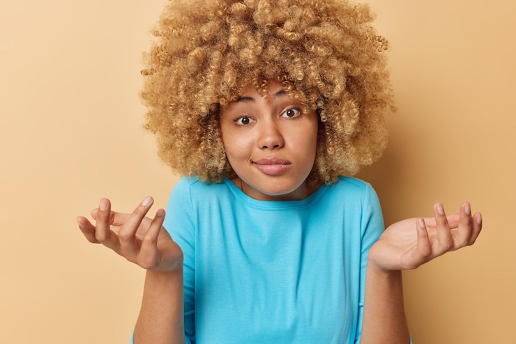 Foto gratuito la foto horizontal de una mujer vacilante con el pelo rizado se encoge de hombros mira con desconcierto se siente confundida viste un jersey azul casual aislado sobre un fondo marrón gestos de chica desorientada con perplejidad