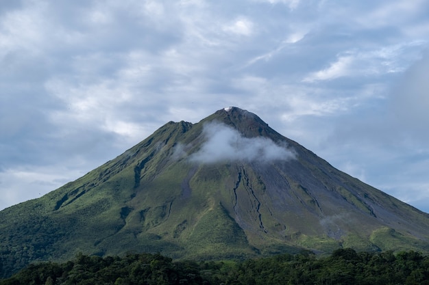 Foto de una impresionante montaña gigante cubierta de bosques, brillando bajo el cielo nublado