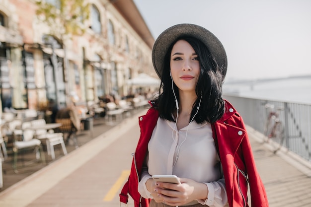 Foto de increíble mujer de cabello negro con expresión de rostro encantador caminando por la ciudad