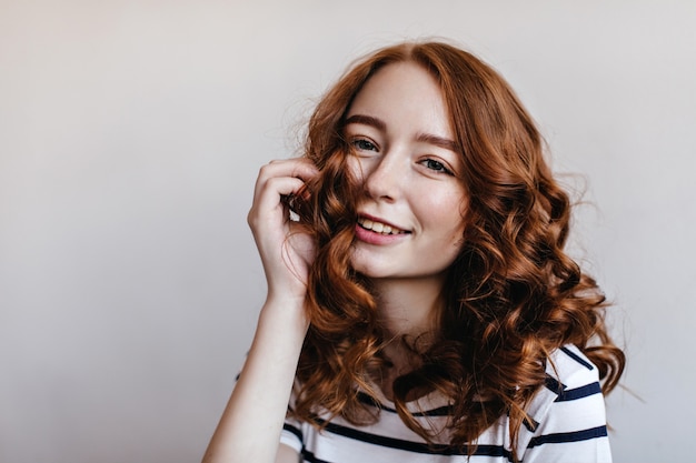 Foto interior de una atractiva chica de jengibre sonriente. Dama europea con estilo en traje de rayas que expresa felicidad.