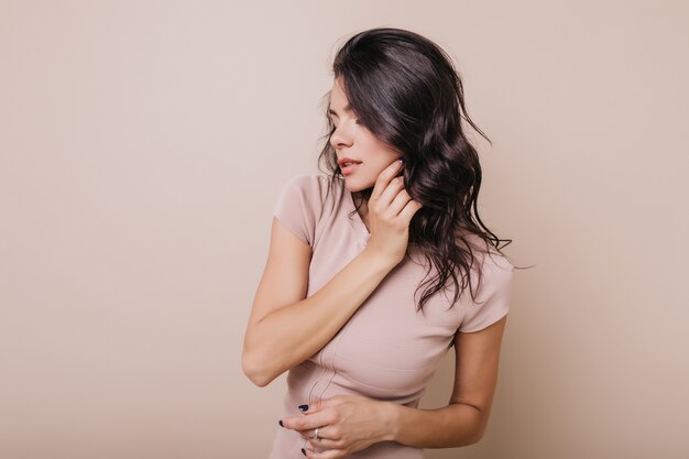 Foto en el interior de una dama bronceada con manicura azul. Chica con cabello ondulado brillante posando de perfil.