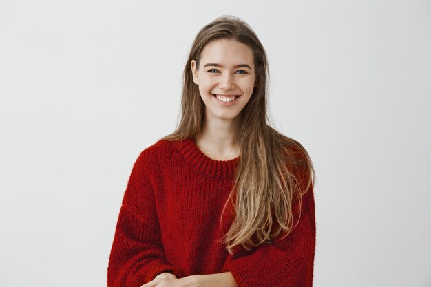 Foto interior de una encantadora mujer europea de aspecto amable con elegante suéter holgado, hablando casualmente con un compañero de trabajo durante el descanso en el trabajo, sonriendo ampliamente, encantada y entusiasmada con la conversación