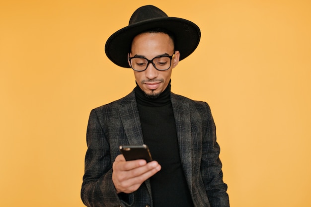 Foto gratuita foto interior de un joven negro con un atuendo magnífico con smartphone. emocional chico africano esperando la llamada con una sonrisa.