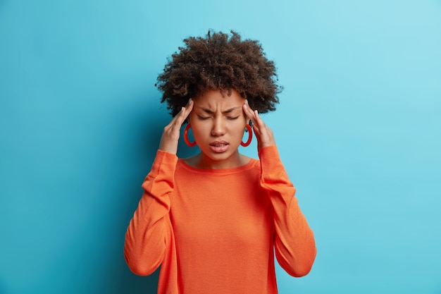 Foto de joven afroamericana frustrada tiene dolor de cabeza mantiene las manos en las sienes sufre migraña insoportable