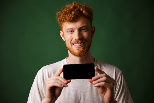 Foto del joven barbudo feliz pelirrojo con camiseta blanca hace una foto en el teléfono inteligente móvil