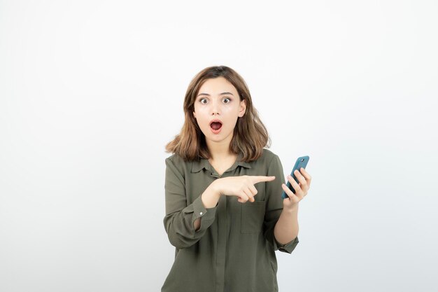 Foto de una joven con un celular parado sobre una pared blanca. foto de alta calidad