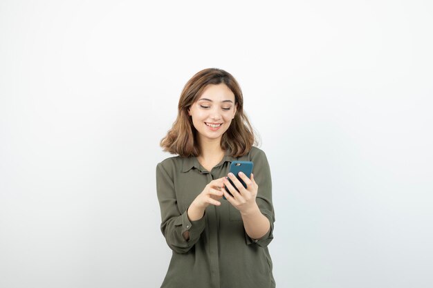 Foto de una joven con un celular parado sobre una pared blanca. foto de alta calidad