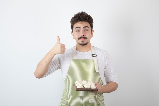 Foto de joven cocinero sosteniendo champiñones crudos en blanco