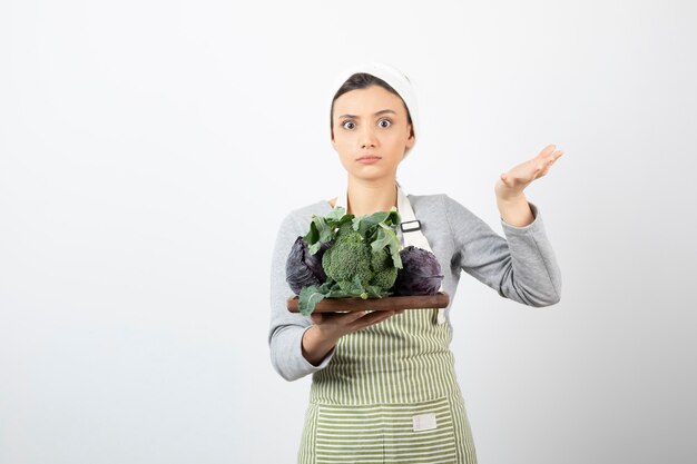 Foto de joven cocinero sosteniendo un plato de repollo y brócoli en blanco