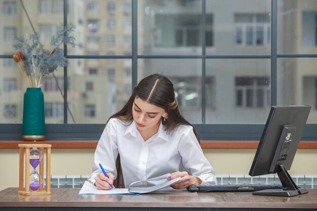 Foto de una joven escribiendo su cuaderno y sentada en el escritorio