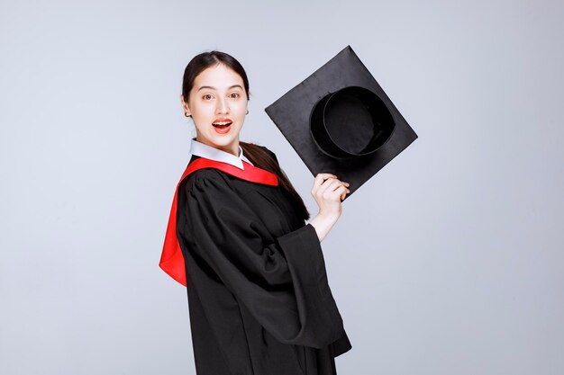 Foto de joven estudiante en bata mostrando su gorro de graduación. Foto de alta calidad