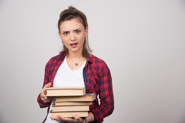 Foto de un joven estudiante sosteniendo una pila de libros.