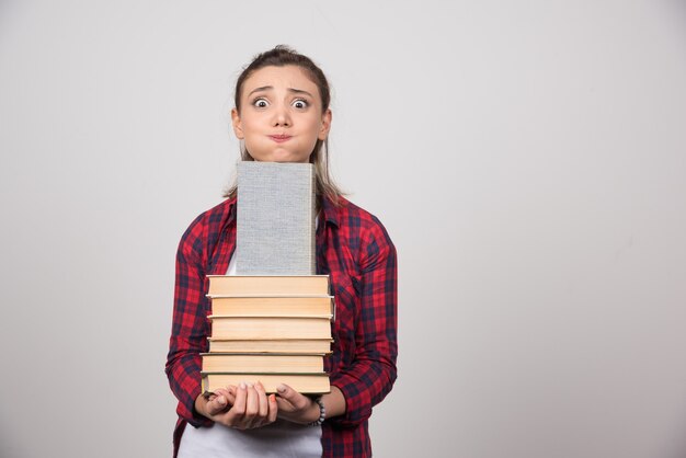 Foto de un joven estudiante sosteniendo una pila de libros.