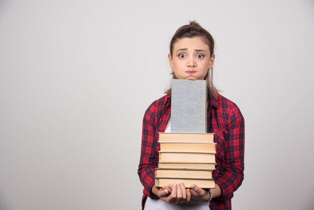 Foto de un joven estudiante sosteniendo una pila de libros.