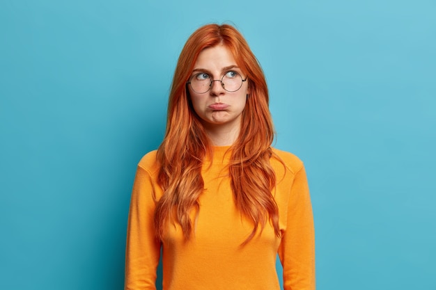 La foto de una joven europea pelirroja ofendida tiene una mirada malhumorada y decepcionada, frunce los labios y mira hacia otro lado el descontento al escuchar palabras desagradables.