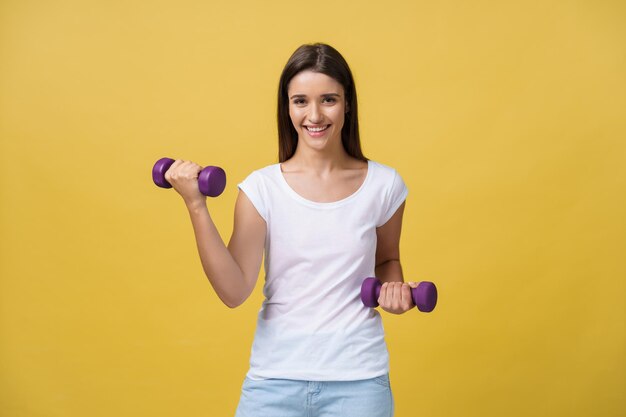Una foto de una joven hermosa y deportiva levantando pesas contra un fondo amarillo