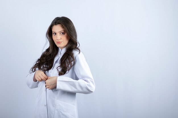 Foto de joven médico en bata blanca de pie en gris.