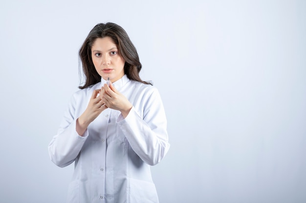 Foto de joven médico con jeringa en gris.