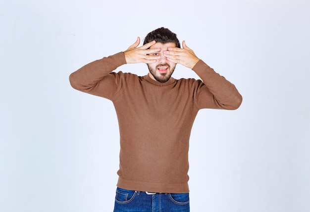 Foto de un joven modelo de pie y tapándose los ojos. Foto de alta calidad