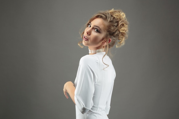 Foto de joven modelo rubia en vestido blanco sobre fondo gris