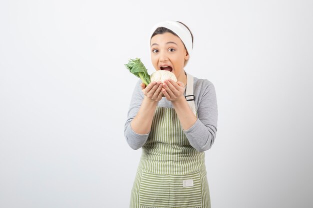 Foto de una joven mujer bonita modelo en delantal comiendo una coliflor