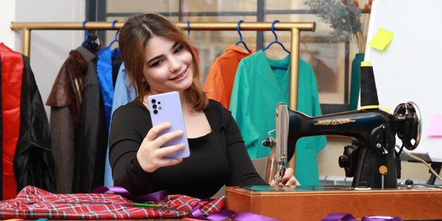 Foto de una joven sastre tomando selfie en el taller