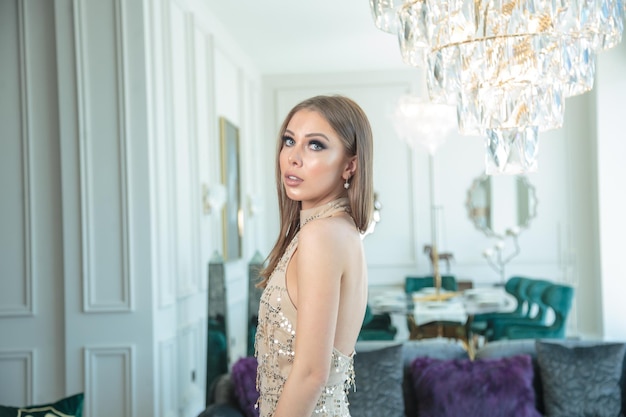 Foto lateral de una joven hermosa parada en la habitación y mirando a la cámara